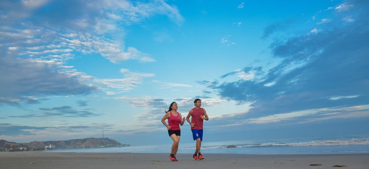 A couple enjoys jogging together along a scenic beach under a bright blue sky.