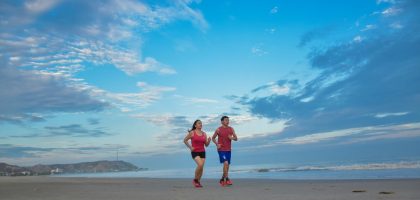 A couple enjoys jogging together along a scenic beach under a bright blue sky.