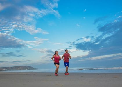 A couple enjoys jogging together along a scenic beach under a bright blue sky.